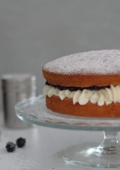 Victoria Sponge Cake with Mascarpone Cream Icing and Blackberry Jam on a glass cake stand