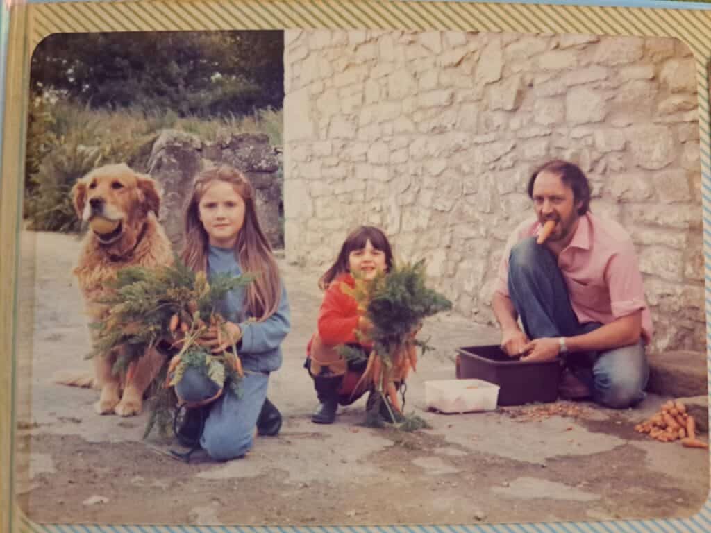 Chloe with her Dad, sister, and dog, outside their house, with a bumper crop of homegrown carrots