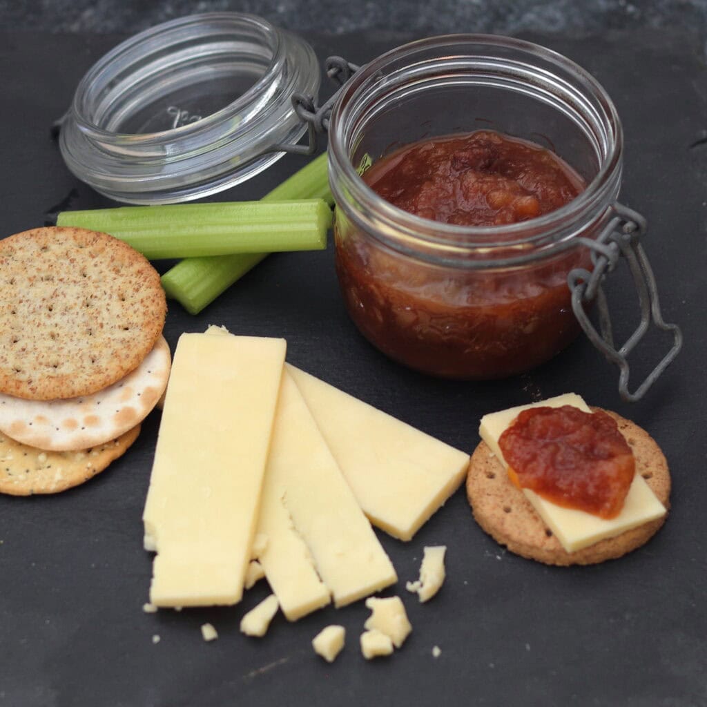 Cheese board with cheddar, biscuits, celery and a jar of apple chutney