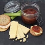 Cheese board with cheddar, biscuits, celery and a jar of apple chutney