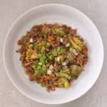 Bowl of beef mince stir fry with diced vegetables and broccoli sprinkle with sliced spring onion and sesame seeds.