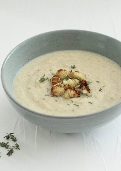 Bowl of cauliflower cheese soup topped with little browned florets of cauliflower and thyme leaves