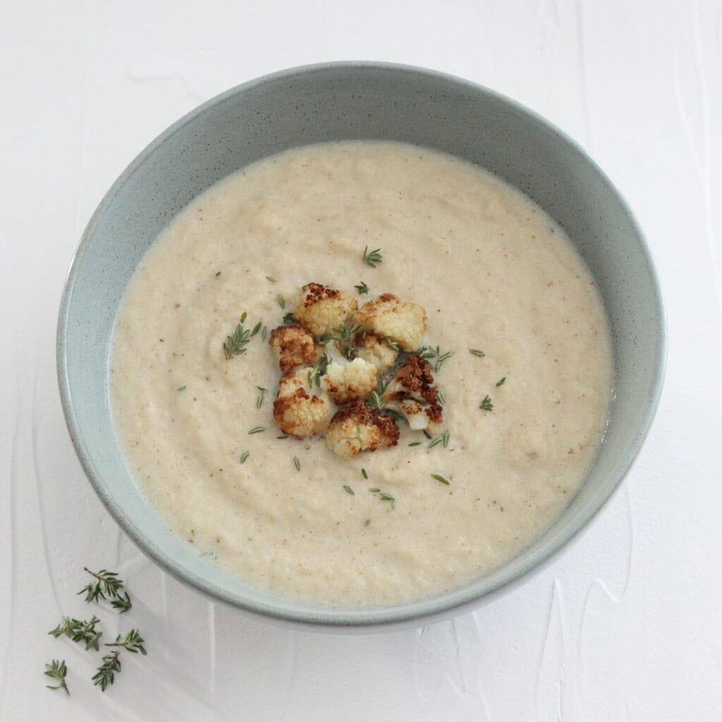Bowl of cauliflower cheese soup topped with little browned florets of cauliflower and thyme leaves