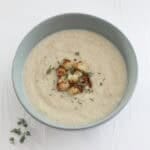Bowl of cauliflower cheese soup topped with little browned florets of cauliflower and thyme leaves