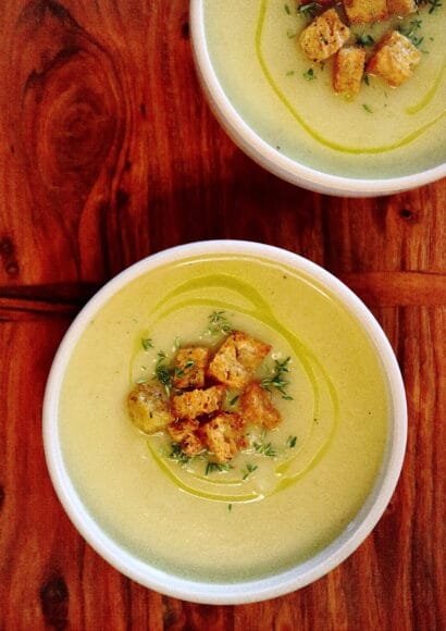 A bowl of smooth, white celeriac soup topped with golden-brown garlic croutons and a sprig of fresh thyme