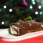 Chocolate sponge filled with cream and rolled into a yuletide christmas chocolate log for your festive season sat infront of a twinkling christmas tree