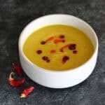 A creamy, vibrant yellow curried parsnip soup in a ceramic bowl, garnished with a bright red drizzle of homemade chilli oil