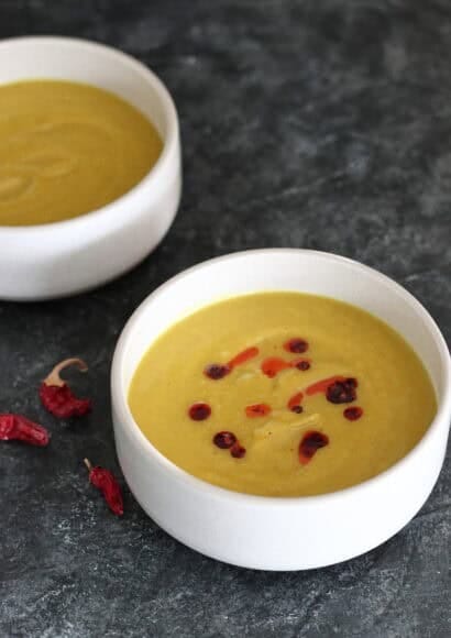 A creamy, vibrant yellow curried parsnip soup in a ceramic bowl, garnished with a bright red drizzle of homemade chilli oil