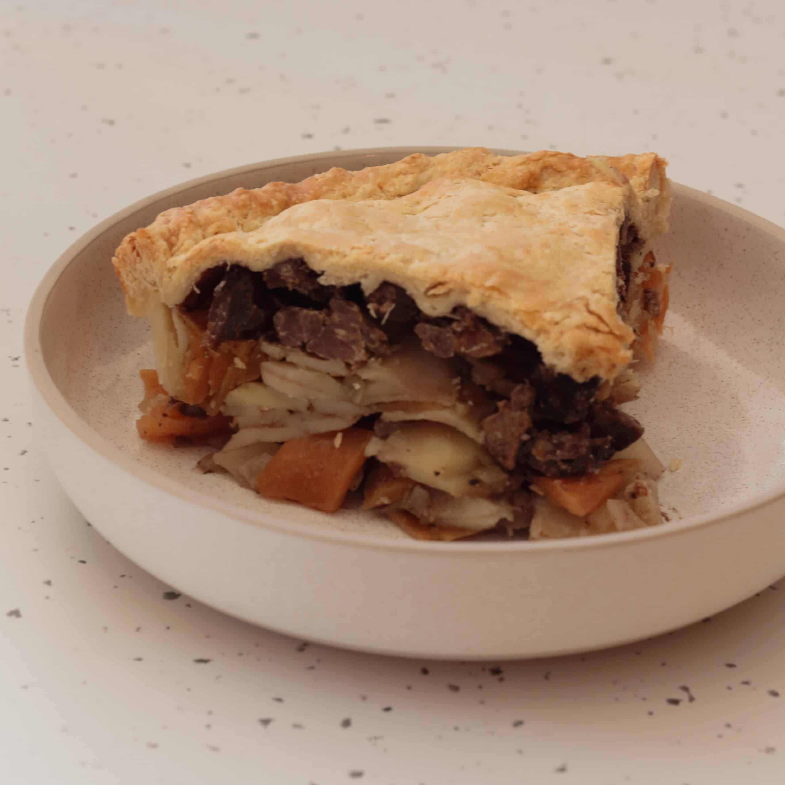 Plate with a slice of pasty pie showing the layers of vegetables, meat and finally the pastry on top