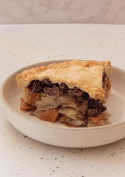 A slice of pasty pie with layers of vegetables, beef and pastry