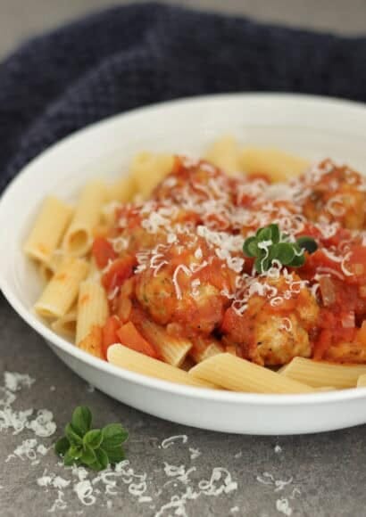 bowl of pasta topped with tomato sauce, chicken meatballs and sprinkled with parmesan and fresh oregano