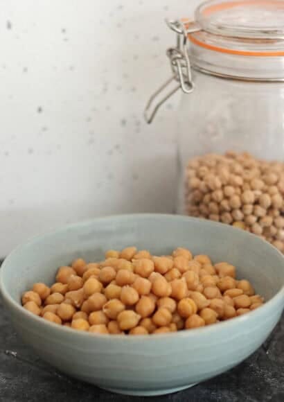bowl of plump chickpeas after no-soak cooking in a pressure cooker next to a jar of dried chickpeas