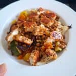 Bowlful of roasted vegetables including cauliflower, beetroot, courgette, carrot and red onions, topped with lentil and spice covered fried halloumi