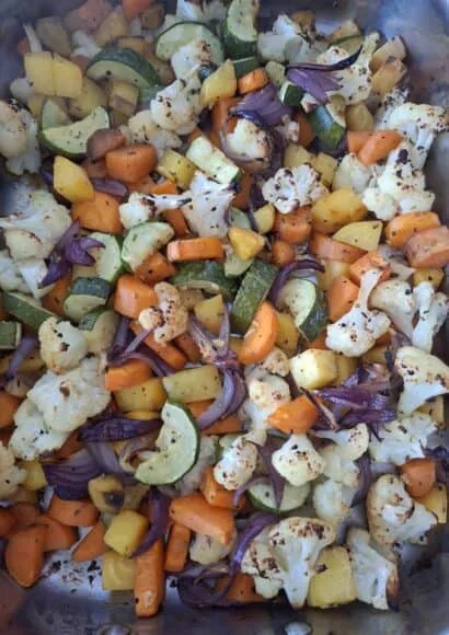 Roasting dish filled with roasted vegetables including cauliflower, sweet potato, carrots, red onions and courgette