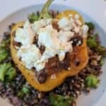 Bowl with quinoa and broccoli salad with walnuts and red onion. Topped with a baked yellow pepper stuffed with chilli and topped with feta cheese