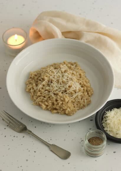 Candlelit table with a bowl of cacio e pepe risotto, a fork, and small dishes of parmesan and of black pepper