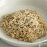 A close up shot of a bowl of creamy cacio e pepe risotto showing the specs of black pepper and plenty of pecorino cheese