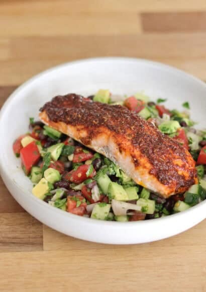 Cajun-spiced salmon fillet resting on a vibrant Mexican-inspired salad with tomato, cucumber,, black beans, red onion, red chilli, coriander, and lime dressing