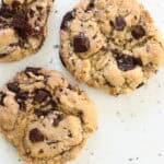 close up of 3 cookies on a worktop showing the chocolate chunks and sprinkling of sea salt on the top