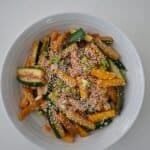 A medium white bowl filled with batons of green and yellow courgette that have been stir-fried in a sauce of soy, hoisin, and sprinkled with sesame seeds.
