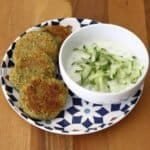 Fresh courgette and chickpea falafels arranged with on a colourful plate with a dipping bowl of tzatziki sauce topped with grated cucumber