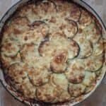 A slim casserole dish full of courgette grain, topped with circles of sliced courgette and browned, melted cheese that has gone crunchy at the edges.