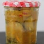A pyramid of six jars filled with courgette chutney. The chutney shows visible courgette pieces, red chilli flecks and a glossy, tangy sauce with warm spices. The jars are stacked neatly, highlighting the texture and colour of the chutney