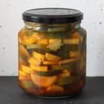A close up of a jar containing slices of yellow and green courgettes in a brine that's dotted with fresh dill