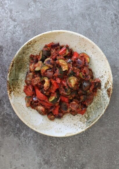A speckled presentation bowl full of colourful ratatouille - including aubergine, courgette, peppers and tomatoes.