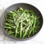 Warm green beans with lemon and parmesan dressing served in a dark grey bowl on a marble worktop, finished with finely grated parmesan, sea salt and black pepper.