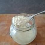Small glass jar of creamy white horseradish sauce with a full spoon of sauce resting on top of it.