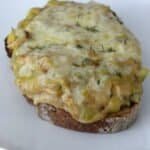 A slice of cheesy leek rarebit on toast with melted sauce oozing over the edge sprinkled with fresh thyme leaves.