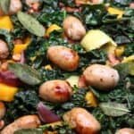 Autumnal sausage and vegetable traybake with squash, leeks, kale and crispy sage leaves in a roasting tray.