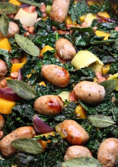 Autumnal sausage and vegetable traybake with squash, leeks, kale and crispy sage leaves in a roasting tray.